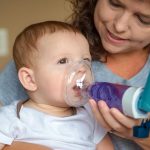 mother using an asthma inhaler with mask attachment on baby